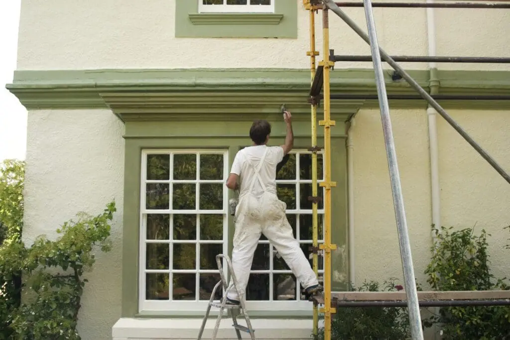 Person painting house exterior on ladder.