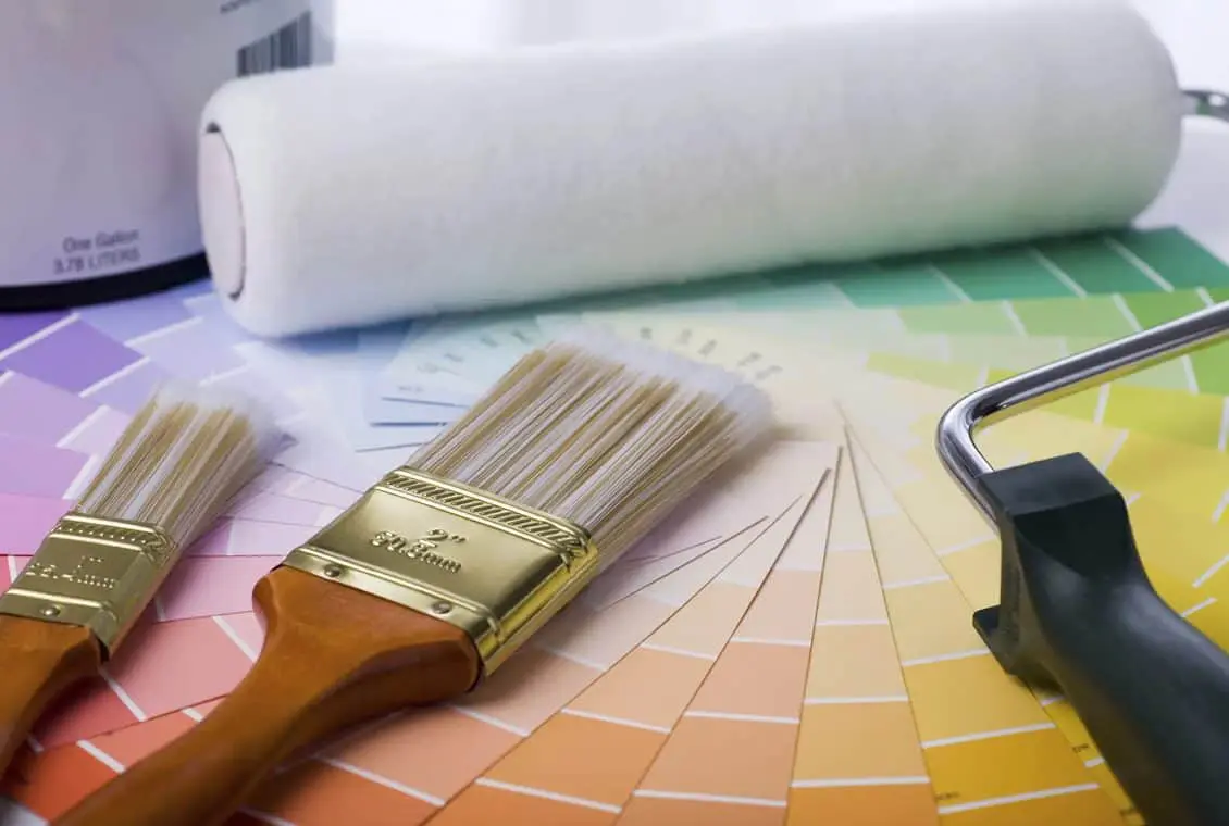 Three paintbrushes, a paint roller, and a can are placed on top of a spread-out color swatch palette displaying various paint colors.