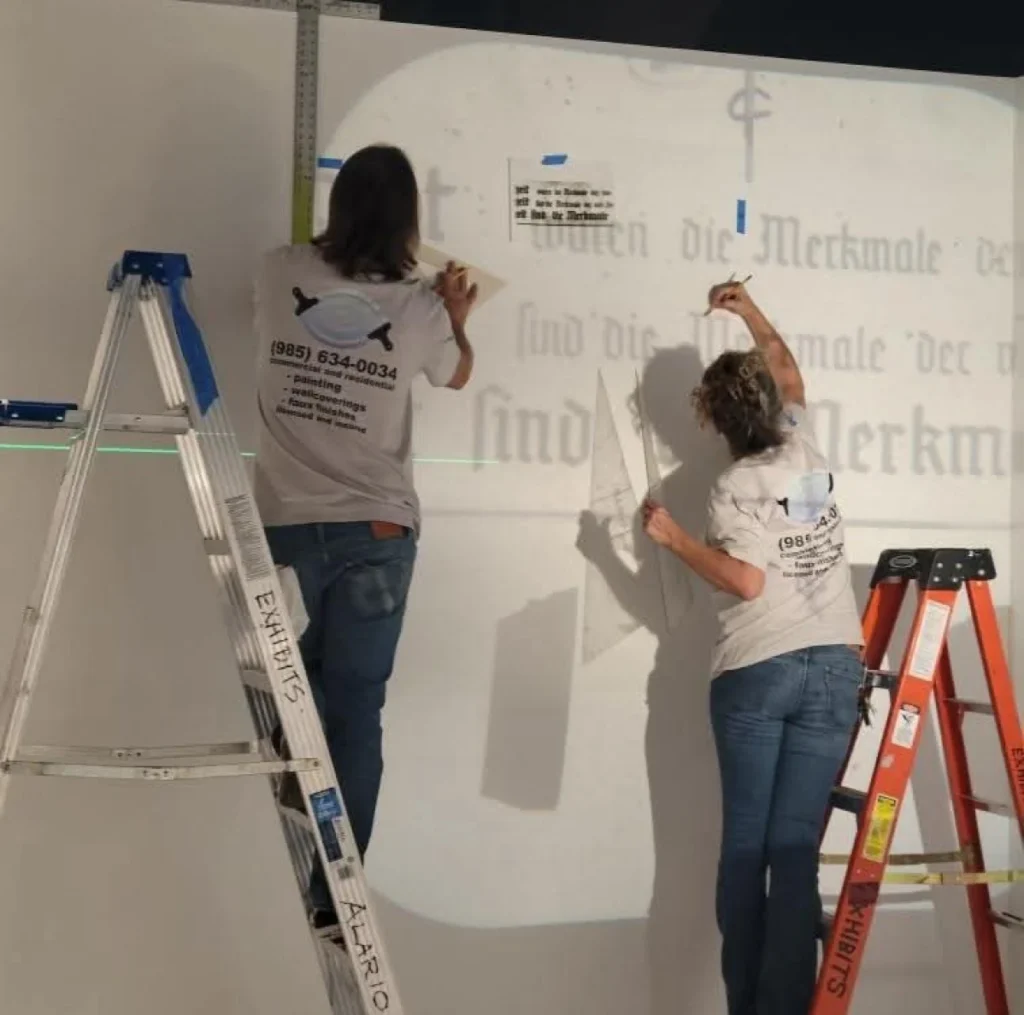 Two people working on wall lettering.